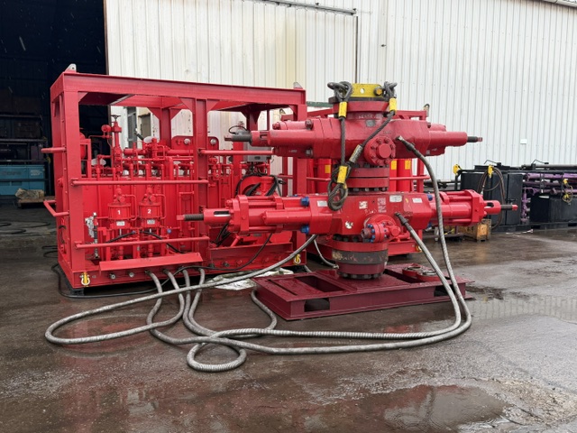 Red blowout preventer (BOP) assembly with hydraulic hoses and control equipment in an oilfield service facility.
